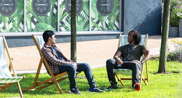 Two males sitting on deck chairs chatting in a green space on a summer day near the Staffordshire University London campus