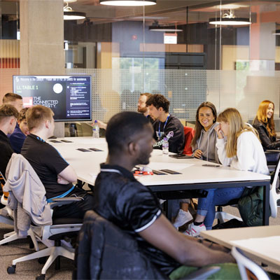 A group of students sitting at tables chatting in a study space in the Catalyst building