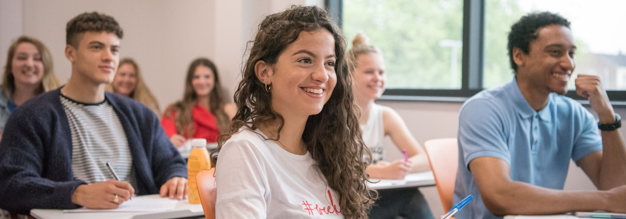 Group of mixed students wearing colourful clothing are sitting at individual desks in a classroom in Staffordshire University's Beacon Building