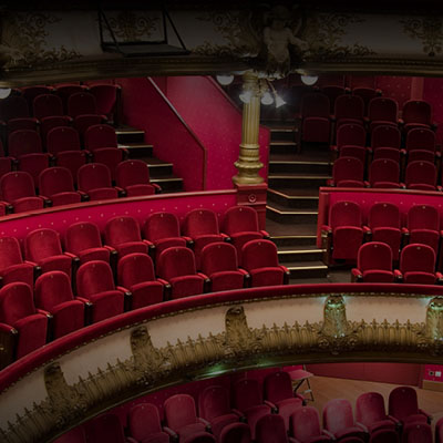 Empty theatre with rows of red seats facing a softly illuminated stage.