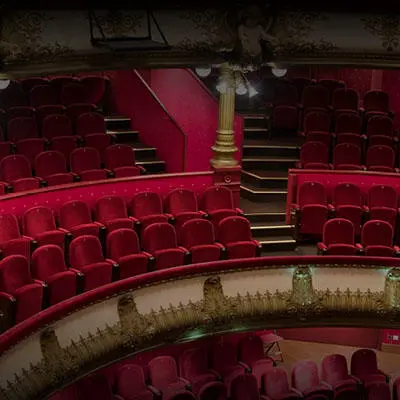 Empty theatre with rows of red seats facing a softly illuminated stage.