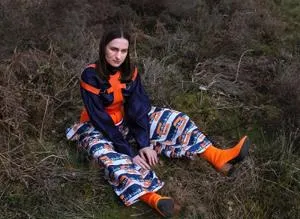 Woman sits outdoors wearing a bold orange, blue and black patterned outfit.