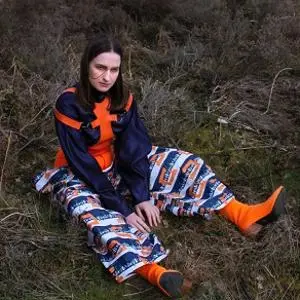 Woman sits outdoors wearing a bold orange, blue and black patterned outfit.