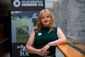 Blonde woman in a green dress stands beside a 'Remembering Srebrenica' display.