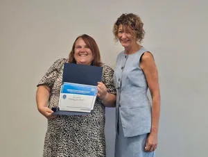 Two smiling women standing together with one holding a framed certificate