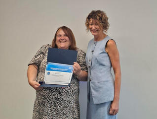 Two smiling women standing together with one holding a framed certificate