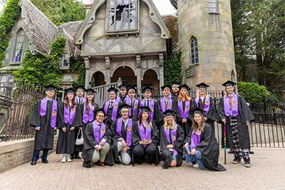 Graduates pictured in their cap and gowns in front of The Curse of Alton Manor