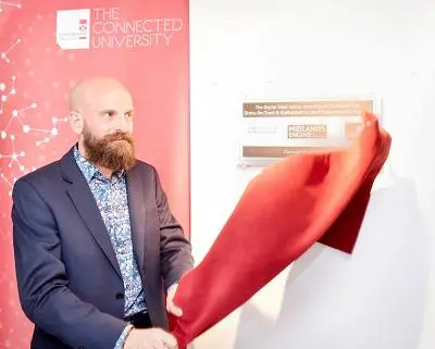 Bald, bearded man unveils a wall display by pulling away a red cloth.