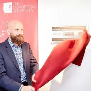 Bald, bearded man unveils a wall display by pulling away a red cloth.
