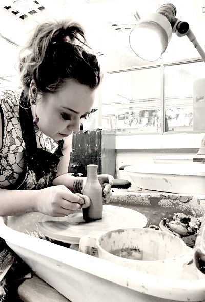 Black-and-white photograph of a woman shaping material at a workshop bench.