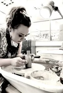 Black-and-white photograph of a woman shaping material at a workshop bench.