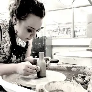 Black-and-white photograph of a woman shaping material at a workshop bench.
