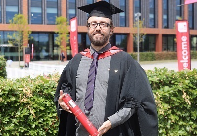 Andy Cartlidge in his graduation robes holding a scroll