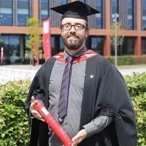Andy Cartlidge in his graduation robes holding a scroll