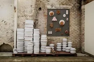 Ceramic installation of stacked white plates and wall-mounted pieces in an industrial gallery.