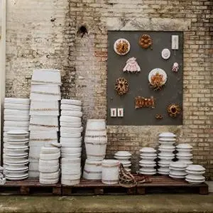Ceramic installation of stacked white plates and wall-mounted pieces in an industrial gallery.