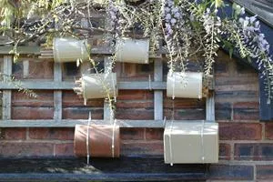 Four small wooden bee hotels hang on a brick wall beneath flowering greenery.