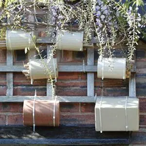 Four small wooden bee hotels hang on a brick wall beneath flowering greenery.