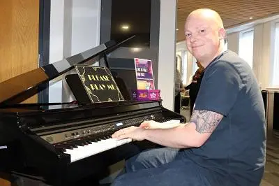 Smiling man sits at a grand piano with sheet music open on the stand.