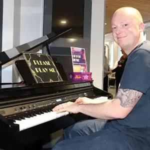 Smiling man sits at a grand piano with sheet music open on the stand.