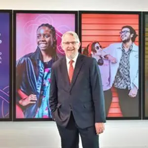 Suited man with hand in pocket stood in front of digital screens