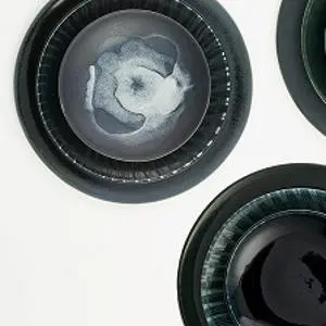 Three dark ceramic bowls with swirling grey and white centres arranged on a pale surface.