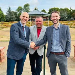 Three men stood outside smiling and shaking hands