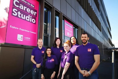 Six career coaches in purple shirts pose outside the magenta Career Studio windows.
