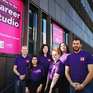 Six career coaches in purple shirts pose outside the magenta Career Studio windows.