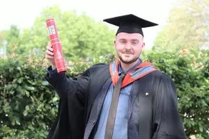 Carl Smith holding a scroll in his graduation robes