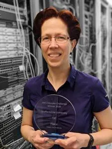 Woman holds a transparent award while standing in front of rows of computer servers.