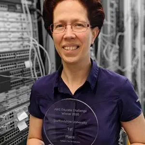 Woman holds a transparent award while standing in front of rows of computer servers.