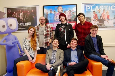 Animation studio team poses together in an office decorated with colourful film posters.