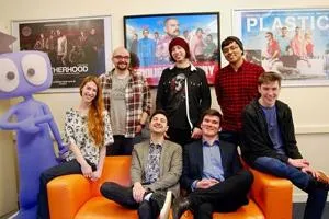 Animation studio team poses together in an office decorated with colourful film posters.