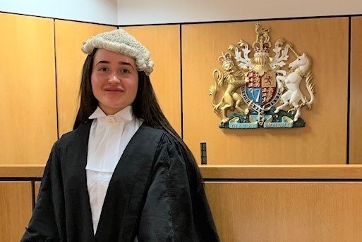 Young woman in a barrister's wig and black gown stands in a courtroom.