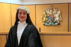Young woman in a barrister's wig and black gown stands in a courtroom.