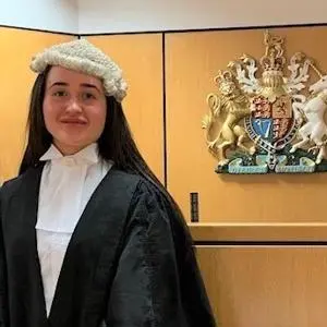 Young woman in a barrister's wig and black gown stands in a courtroom.