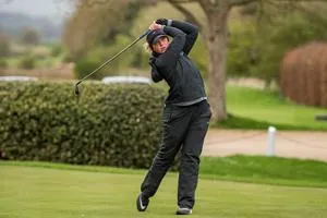 Woman golfer in black swings a club on a green course.