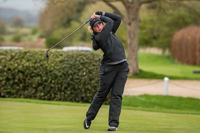 Woman golfer in black swings a club on a green course.
