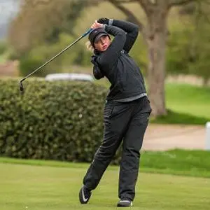 Woman golfer in black swings a club on a green course.