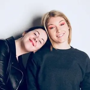 Two young women pose together, one resting her head on the other's shoulder.