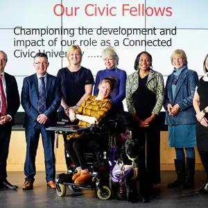 Six Civic Fellows, including a wheelchair user, pose beneath a presentation screen.