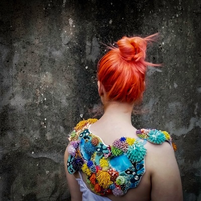 Red-haired woman seen from behind wearing a garment decorated with colourful textured sea forms.