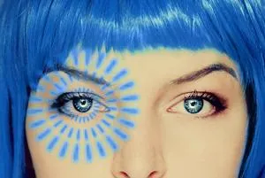 Close-up of a blue-haired woman with a blue and yellow sun design painted around one eye.