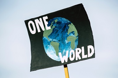 Handmade protest sign reading 'ONE WORLD' around a painted globe.
