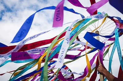 Colourful fabric ribbons stream from a circular frame against a bright blue sky.