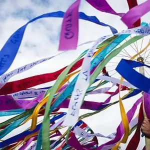 Colourful fabric ribbons stream from a circular frame against a bright blue sky.