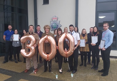 Group holds certificates and large rose-gold balloons forming the number 300.