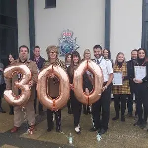Group holds certificates and large rose-gold balloons forming the number 300.