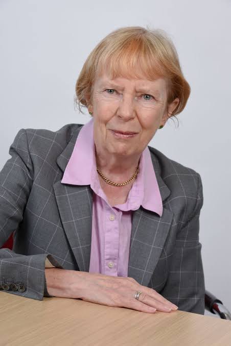 A woman with short light coloured hair wearing a shirt and blazer smiling at the camera